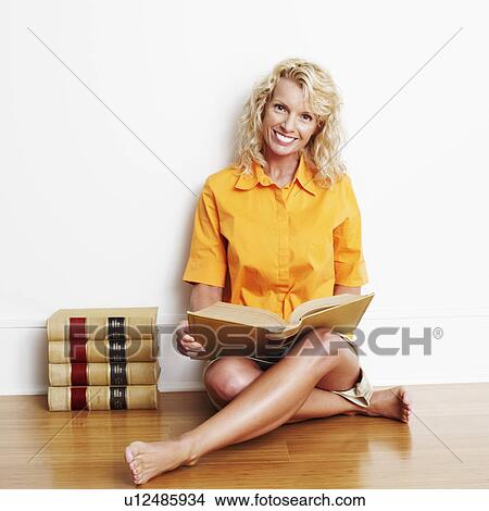 Picture - Portrait of a mid adult woman sitting cross-legged on the floor with a book and smiling. Fotosearch