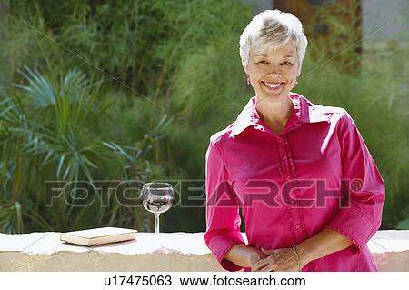 Stock Image - Portrait of a senior woman leaning against a wall on a terrace. Fotosearch