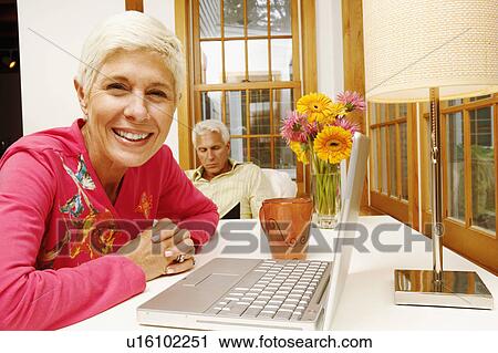 Stock Image - Portrait of a senior woman smiling with a mature man sitting behind her. Fotosearch