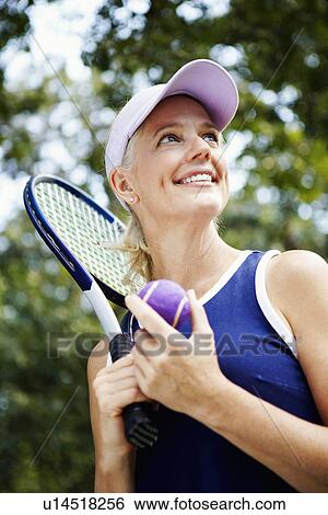Stock Photograph - Low angle view of a mature woman holding a tennis racket and a tennis ball. Fotosearch