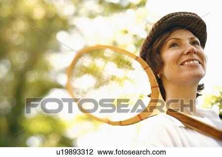 Low angle view of a mid adult woman holding a tennis racket and smiling View Large Photo Image Stock Image - Low angle view of a mid adult woman holding a tennis racket and smiling. Fotosearch