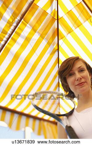 Low angle view of a mid adult woman holding a tennis racket and smiling View Large Photo Image Stock Photo - Low angle view of a mid adult woman holding a tennis racket and smiling. Fotosearch