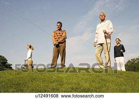 Stock Photo - Low angle view of two men and two women standing at a golf course. Fotosearch
