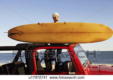 Mature woman standing in a sports utility vehicle holding a surfboard View Large Photo Image Stock Image - Mature woman standing in a sports utility vehicle holding a surfboard. Fotosearch