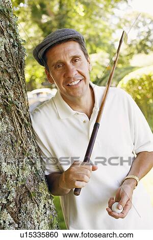 Stock Image - Portrait of a mature man holding a golf club and a golf ball. Fotosearch