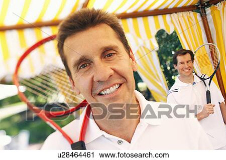 Portrait of a mature man holding a tennis racket and a mid adult man standing behind him View Large Photo Image Stock Image - Portrait of a mature man holding a tennis racket and a mid adult man standing behind him. Fotosearch