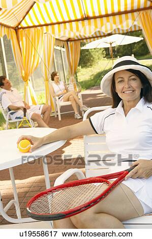 Stock Photo - Portrait of a mature woman holding a tennis ball and a tennis racket. Fotosearch