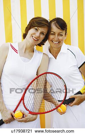 Stock Image - Portrait of a mid adult woman and a mature woman holding tennis rackets and tennis balls. Fotosearch