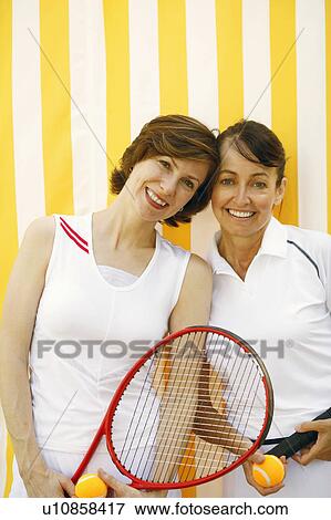 Stock Photo - Portrait of a mid adult woman and a mature woman holding tennis rackets and tennis balls. Fotosearch