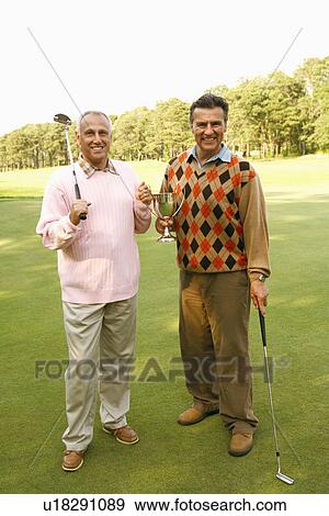 Stock Photo - Portrait of two mature men holding a trophy and golf clubs. Fotosearch