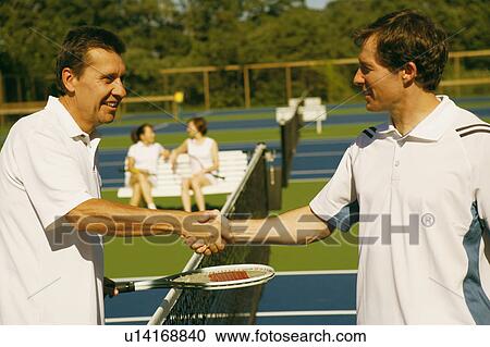 Stock Image - Side profile of a mature man shaking hands with a mid adult man on a tennis court. Fotosearch