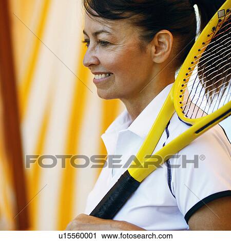 Stock Image - Side profile of a mature woman holding a tennis racket and smiling. Fotosearch