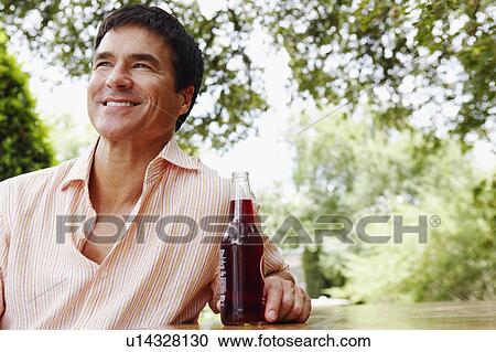 Stock Image - Close-up of a mature man holding a bottle of red wine and smiling. Fotosearch