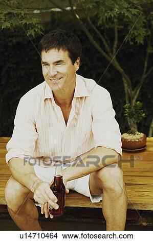 Close-up of a mature man sitting on a table and holding a bottle of red wine View Large Photo Image Picture - Close-up of a mature man sitting on a table and holding a bottle of red wine. Fotosearch