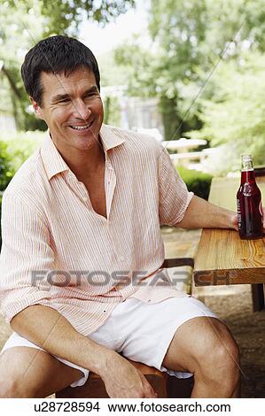 Close-up of a mature man sitting on a stool and smiling View Large Photo Image Picture - Close-up of a mature man sitting on a stool and smiling. Fotosearch