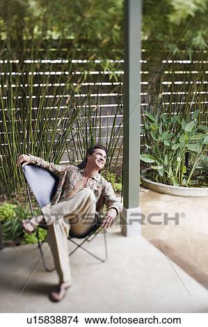 Picture - Mature man sitting on a chair on a porch. Fotosearch
