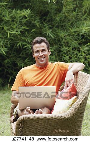 Stock Photo - Mature man with a laptop sitting on a couch. Fotosearch
