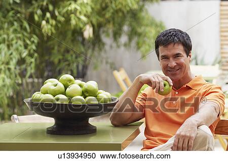 Stock Image - Portrait of a mature man holding a granny smith apple and smiling. Fotosearch