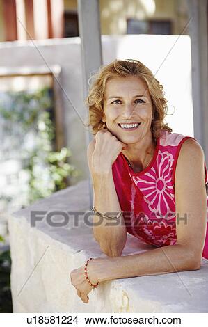 Portrait of a mature woman leaning against a wall with her hand on her chin and smiling View Large Photo Image Picture - Portrait of a mature woman leaning against a wall with her hand on her chin and smiling. Fotosearch