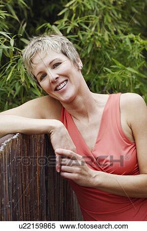 Stock Photography - Portrait of a mature woman leaning against a fence and smiling. Fotosearch