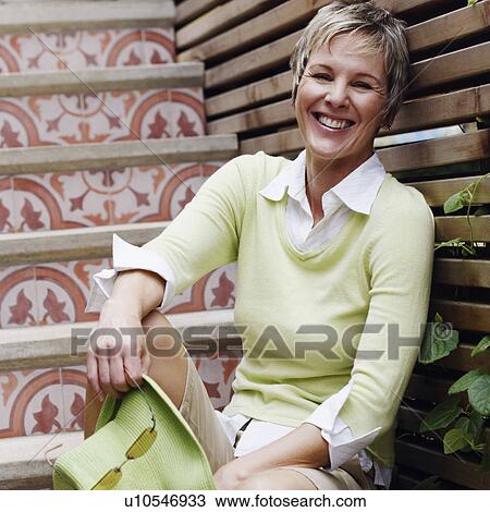 Stock Image - Portrait of a mature woman sitting on a staircase and smiling. Fotosearch