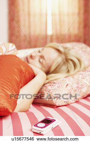 Stock Photograph - Close-up of a flip phone with a mature woman sleeping on the bed. Fotosearch