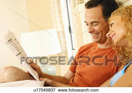 Stock Photo - Close-up of a mature couple reclining on the bed and reading newspapers. Fotosearch