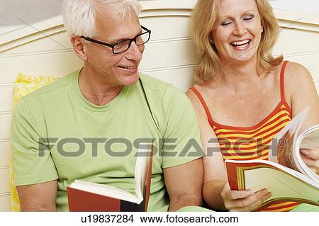 Picture - Close-up of a mature couple sitting on the bed and smiling. Fotosearch