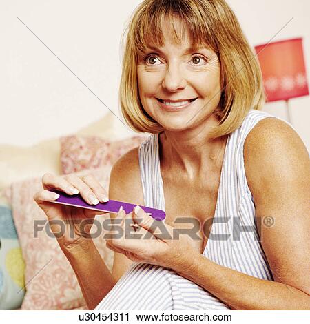 Close-up of a mature woman sitting on the bed and filing her fingernails with a nail file View Large Photo Image Stock Image - Close-up of a mature woman sitting on the bed and filing her fingernails with a nail file. Fotosearch