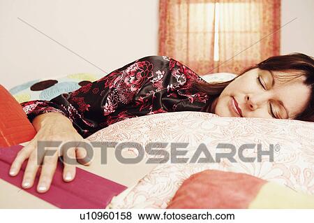 Stock Photo - Close-up of a mature woman sleeping on the bed with her hand on an open book. Fotosearch