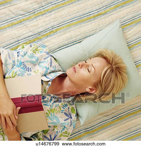 Stock Photo - High angle view of a mature woman sleeping on the bed with a book. Fotosearch