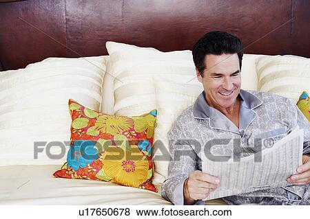 Mature man lying on the bed and reading a newspaper View Large Photo Image Stock Photo - Mature man lying on the bed and reading a newspaper. Fotosearch