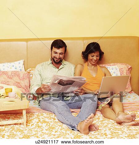 Mature man reading a newspaper with a mature woman using a laptop beside him View Large Photo Image Stock Photo - Mature man reading a newspaper with a mature woman using a laptop beside him. Fotosearch