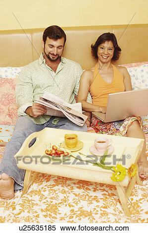 Mature man reading a newspaper with a mature woman using a laptop on the bed View Large Photo Image Stock Photography - Mature man reading a newspaper with a mature woman using a laptop on the bed. Fotosearch