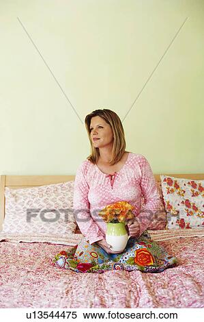 Stock Photography - Mature man sitting on the bed and holding a pitcher of flowers. Fotosearch