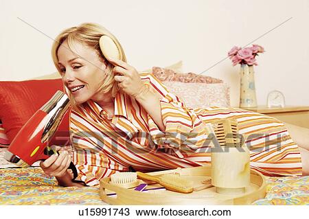 Mature woman lying on the bed and drying her hair with a hair dryer View Large Photo Image Stock Image - Mature woman lying on the bed and drying her hair with a hair dryer. Fotosearch