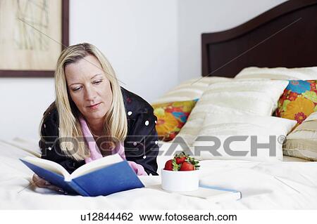 Mature woman lying on the bed reading a book View Large Photo Image Stock Image - Mature woman lying on the bed reading a book. Fotosearch