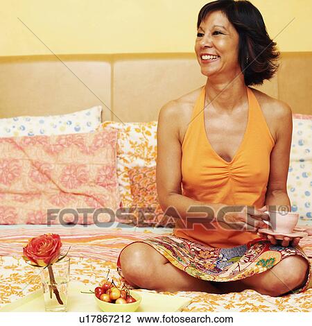Mature woman sitting on the bed and holding a cup of tea View Large Photo Image Stock Image - Mature woman sitting on the bed and holding a cup of tea. Fotosearch