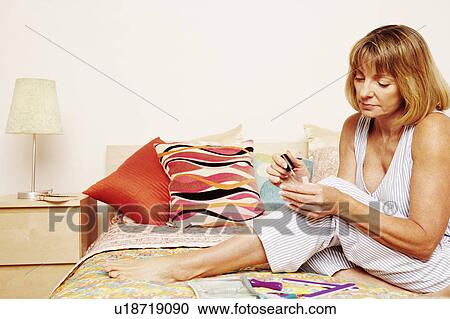 Mature woman sitting on the bed applying nail polish View Large Photo Image Stock Image - Mature woman sitting on the bed applying nail polish. Fotosearch