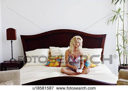 Stock Photo - Mid adult woman sitting on the bed with a bowl full of grapes and smiling. Fotosearch