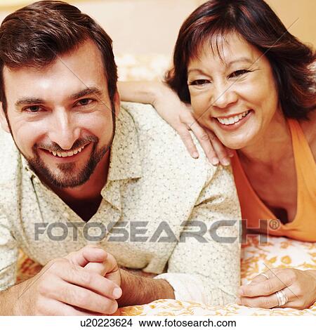 Picture - Portrait of a mature couple lying on the bed and smiling. Fotosearch