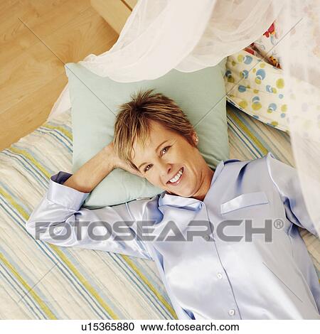 Stock Image - Portrait of a mature woman lying in bed and smiling. Fotosearch