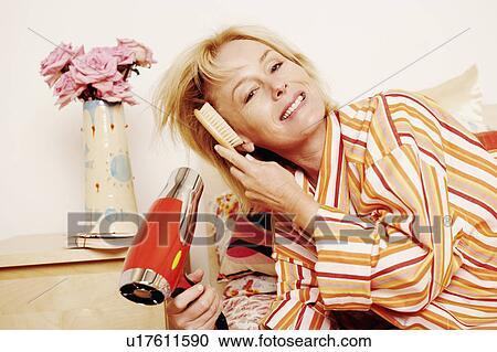 Portrait of a mature woman lying in bed and drying her hair with a hair dryer View Large Photo Image Stock Image - Portrait of a mature woman lying in bed and drying her hair with a hair dryer. Fotosearch