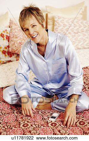 Portrait of a mature woman sitting on the bed and listening to an MP3 player View Large Photo Image Stock Image - Portrait of a mature woman sitting on the bed and listening to an MP3 player. Fotosearch