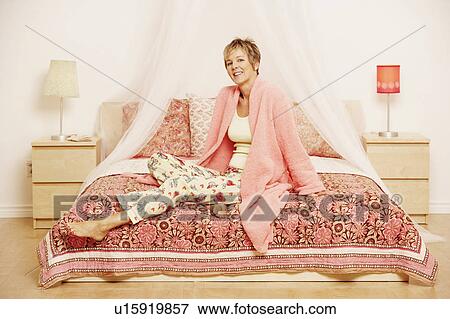 Stock Photo - Portrait of a mature woman sitting on the bed. Fotosearch