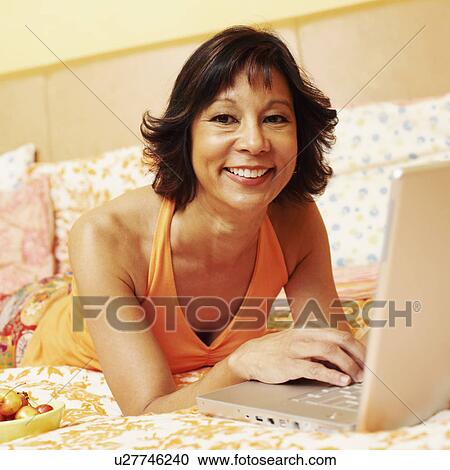 Stock Image - Portrait of a mature woman smiling and using a laptop. Fotosearch
