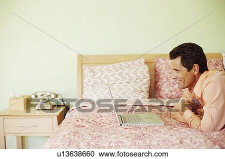 Side profile of a mature man lying on the bed in front of a laptop and smiling View Large Photo Image Stock Image - Side profile of a mature man lying on the bed in front of a laptop and smiling. Fotosearch