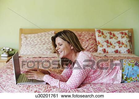 Side profile of a mature woman lying on the bed and using a laptop View Large Photo Image Stock Image - Side profile of a mature woman lying on the bed and using a laptop. Fotosearch