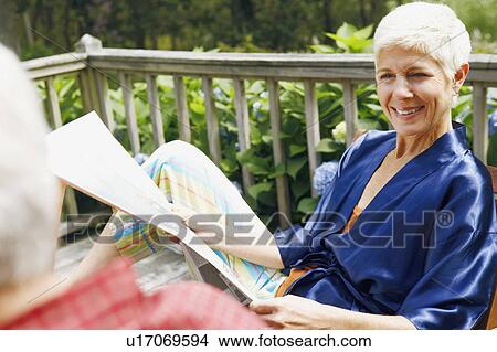 Picture - Close-up of a senior woman holding a newspaper and looking at a mature man. Fotosearch