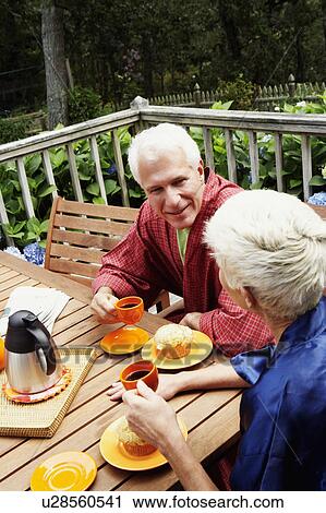 Stock Image - Mature man and a senior woman sitting at the table and talking to each other. Fotosearch